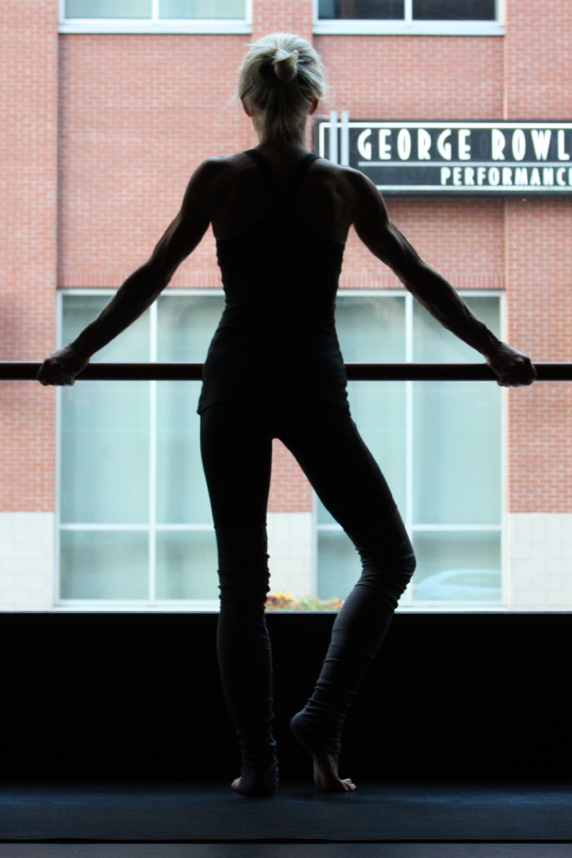 girl standing on natural green yoga mat and looking out a window before yoga class